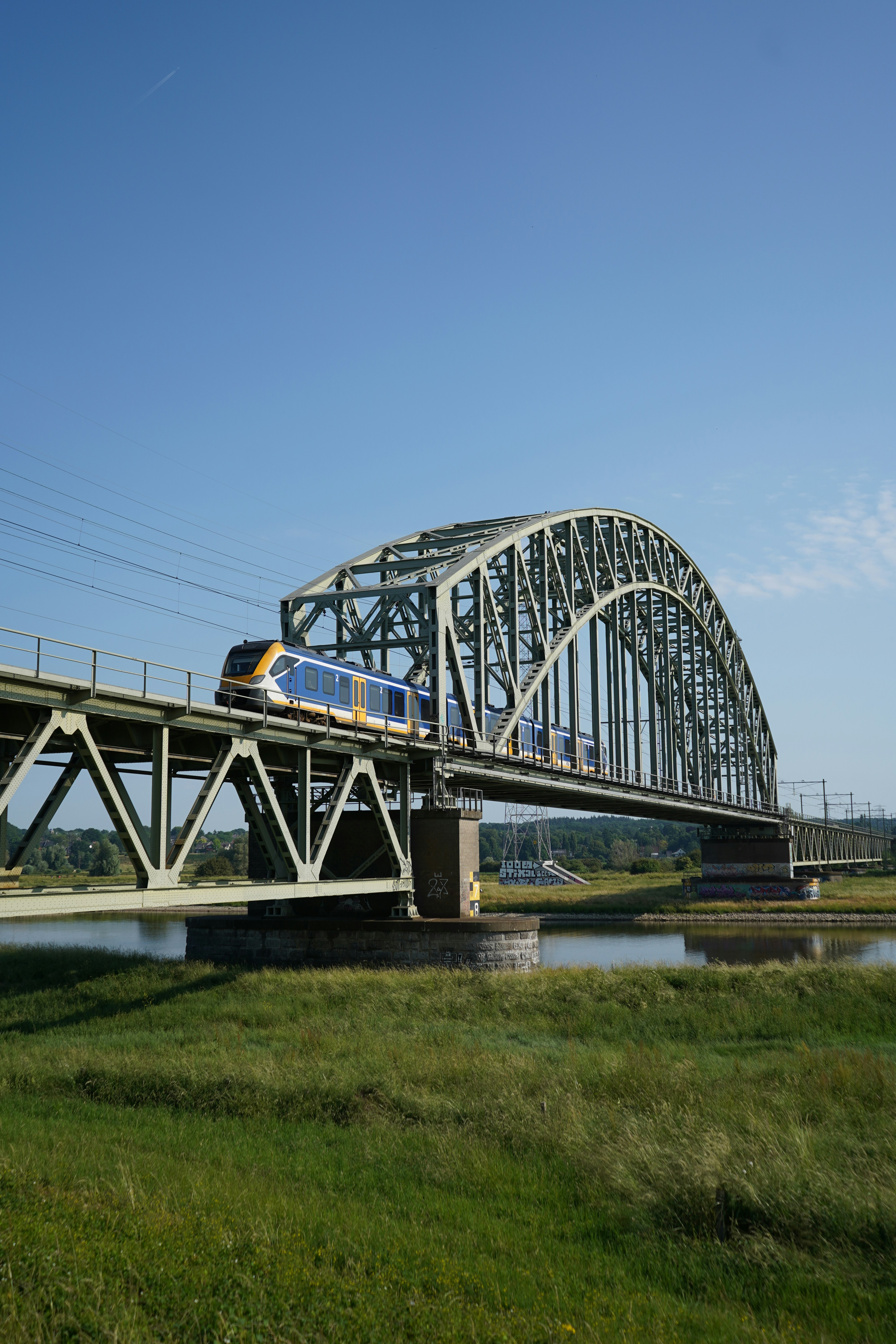 Nederlandse Spoorwegen trein op iconische stalen boogbrug over water, representatief voor SafeU's expertise in Nederlandse spoorweginfrastructuur