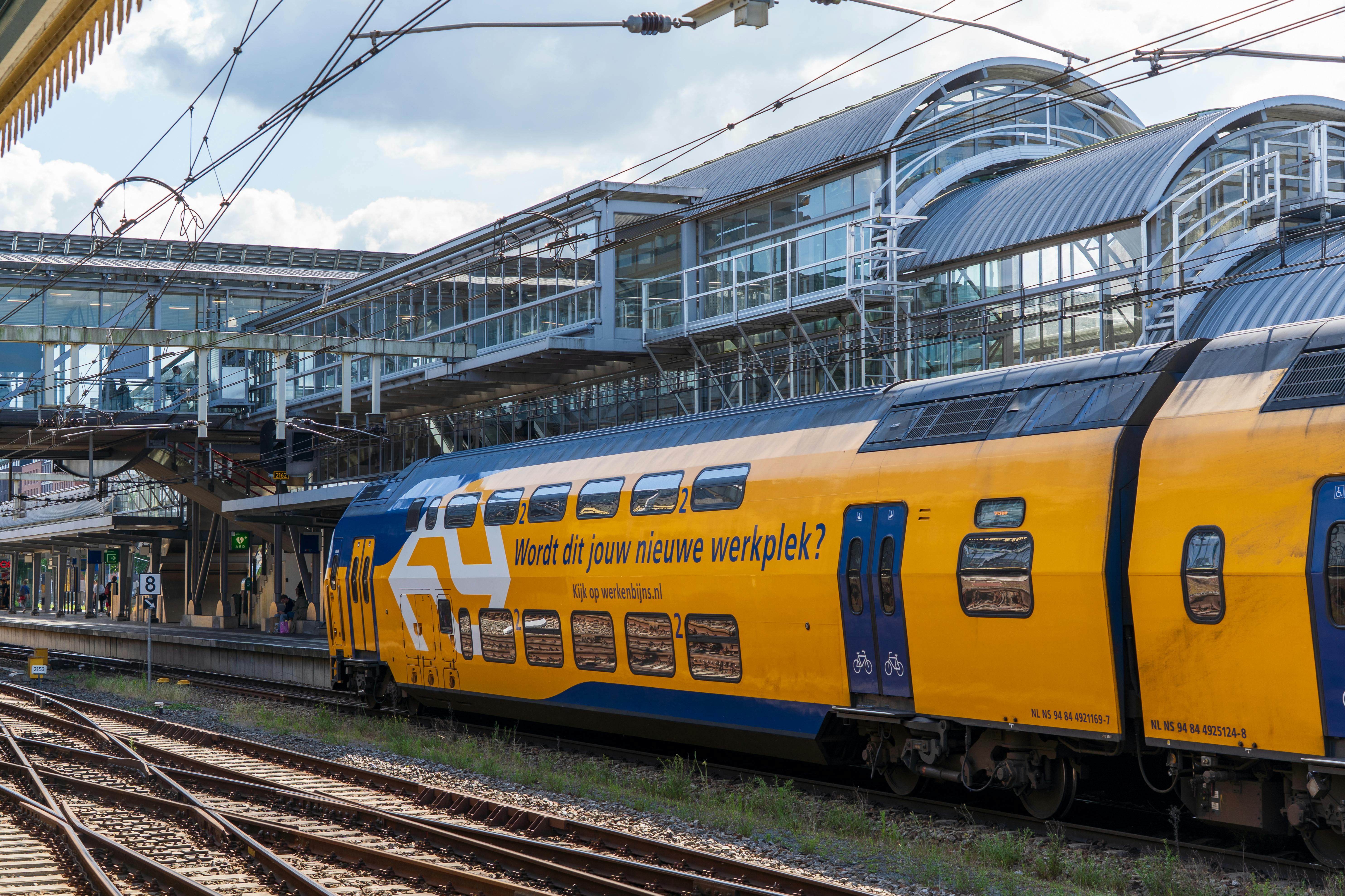 Moderne NS dubbeldekker trein bij eigentijds station met glazen architectuur, werkplek voor veiligheidsprofessionals